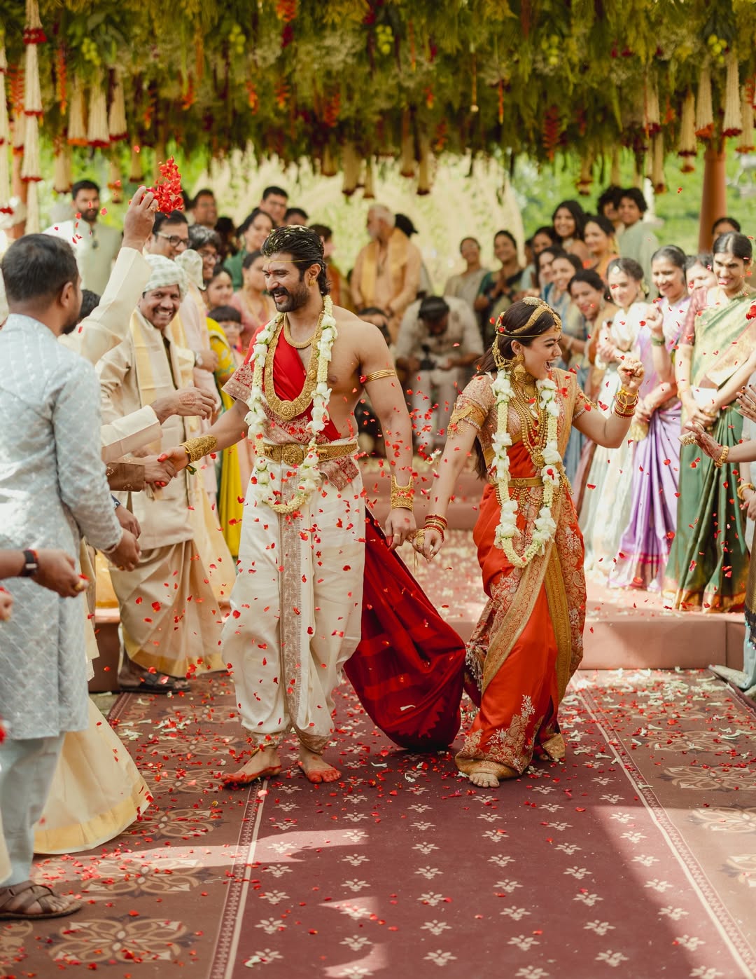 Vijay Deverakonda and Rashmika Mandanna walking together as guests shower rose petals at the Virosh wedding mandap